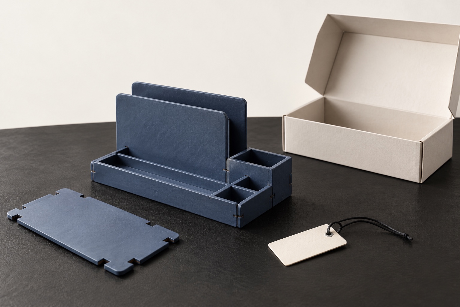 A slate flat-pack desk organizer, a separate matching panel and a blank reservation tag beside an empty ivory shipping box.